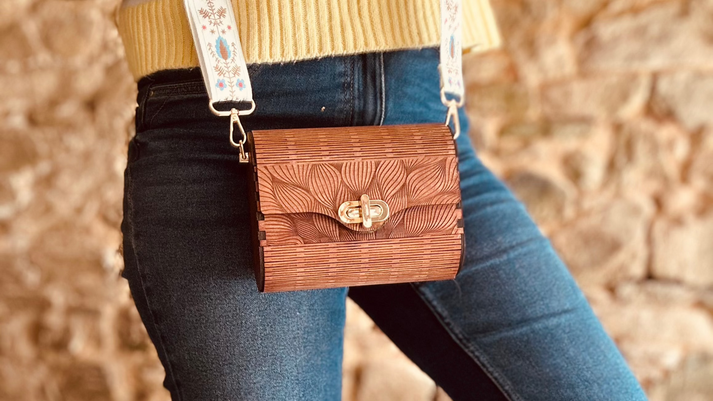 Le Sac en Bois Vivi de Le Bois Elégant, un modèle compact de sac en bois élégant, est porté avec une sangle décorative, mettant en avant son artisanat unique et son design floral.