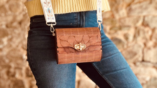 Le Sac en Bois Vivi de Le Bois Elégant, un modèle compact de sac en bois élégant, est porté avec une sangle décorative, mettant en avant son artisanat unique et son design floral.
