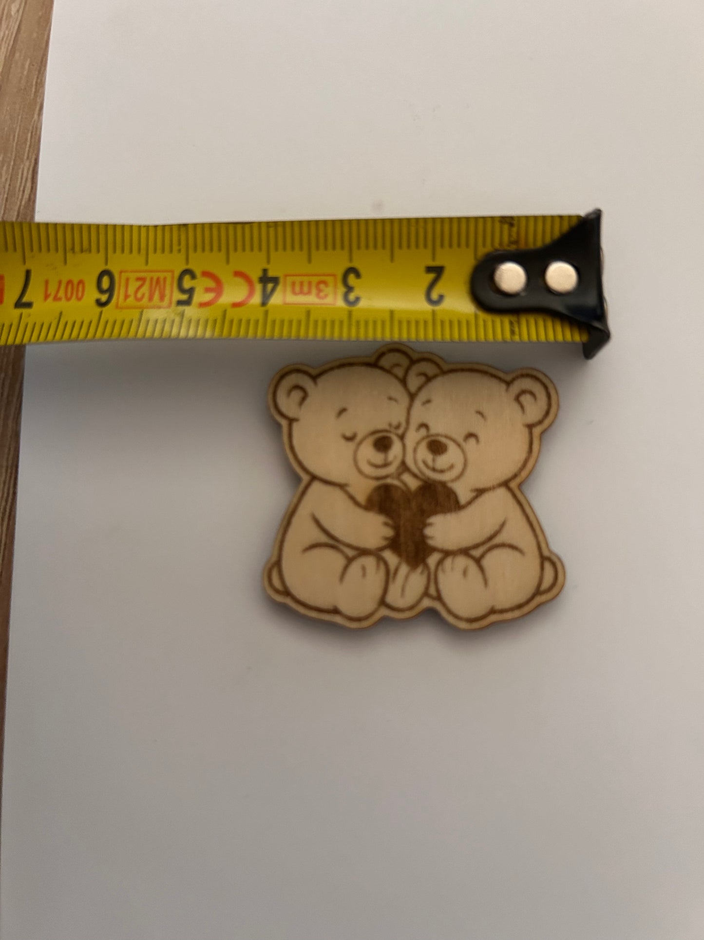 Photo d'un ourson du Câlin de Poche de Le Bois Elégant placé à côté d'un mètre ruban, illustrant sa petite taille pratique. Ce câlin de poche est un excellent moyen d'apporter de la douceur et du réconfort partout où vous allez. calin de poche, pockethug