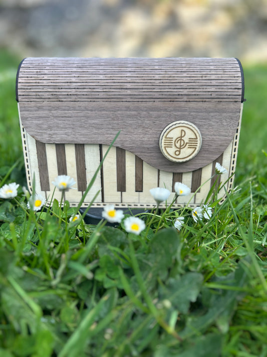 Sac en bois design 'Sac en Bois Piano' de Le Bois Elégant, posé sur l'herbe entouré de fleurs, illustrant l'ARTISANAT et le style unique d'un sac en bois.