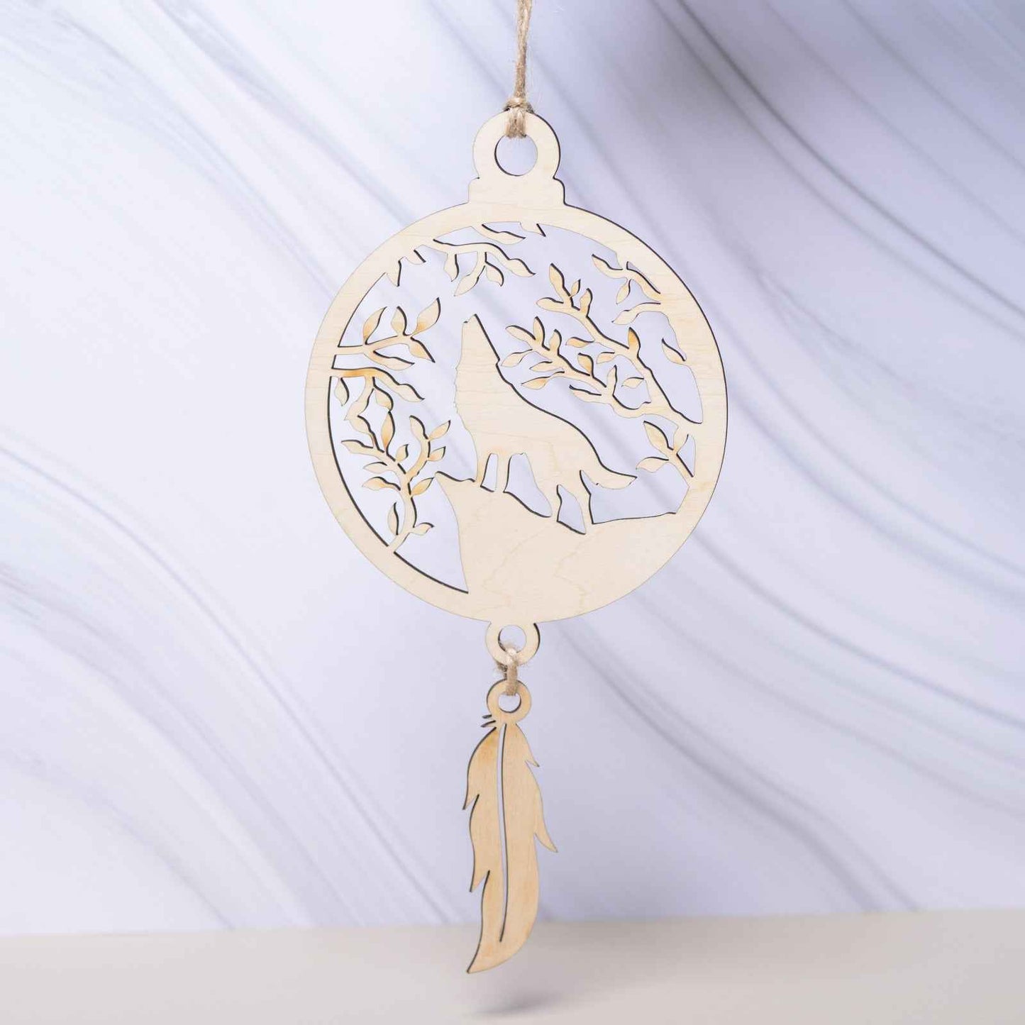 Attrape-rêves en bois de la marque Le Bois Elégant, avec des plumes et perles, suspendu dans un décor naturel.